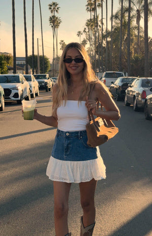 girl wearing a mid-wash denim mini skirt with white ruffle details paired with a white  tube crop top