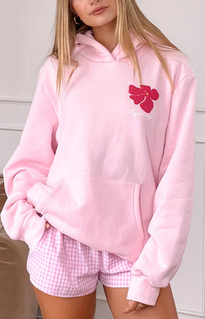 blonde model wearing a baby pink hoodie with a pink flower graphic detail and front pocket