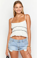 brunette model wearing a white cropped top with contrast black stitching and gathered details